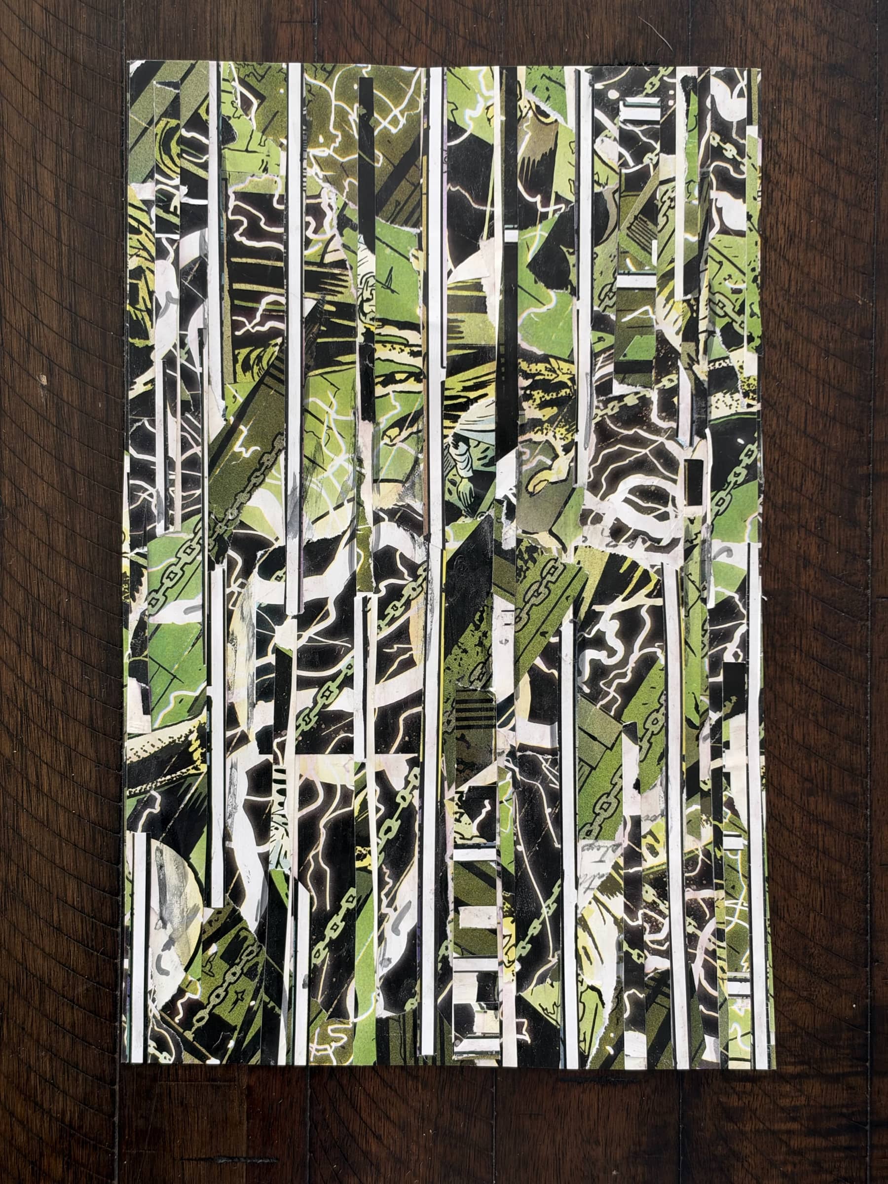A vertical paper collage made from narrow strips of green, black, and white Frankenstein comic imagery, photographed on a dark wooden surface.